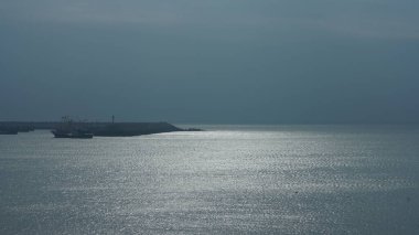 Bulutlu bir günde üzerinde yüzen balıkçı teknesinin olduğu huzurlu deniz manzarası.