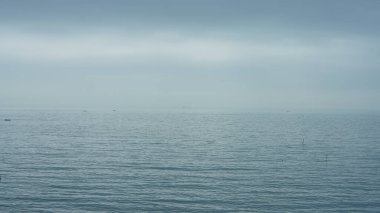 Bulutlu bir günde üzerinde yüzen balıkçı teknesinin olduğu huzurlu deniz manzarası.