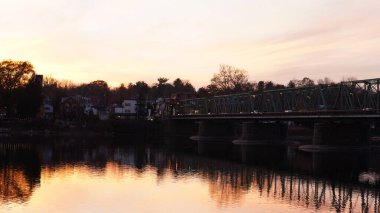 Eski bir rion çerçevesi nehir üzerinde köprü manzarası ve arka planda günbatımı gökyüzü.