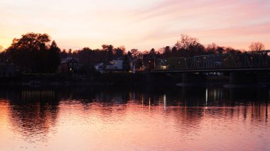 Eski bir rion çerçevesi nehir üzerinde köprü manzarası ve arka planda günbatımı gökyüzü.