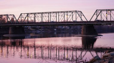 Eski bir rion çerçevesi nehir üzerinde köprü manzarası ve arka planda günbatımı gökyüzü.