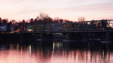 Eski bir rion çerçevesi nehir üzerinde köprü manzarası ve arka planda günbatımı gökyüzü.