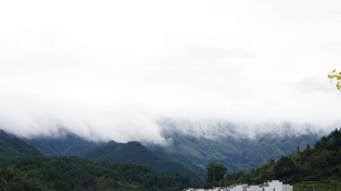 Yeşil ormanlı güzel dağlar ve yağmurlu günlerde arka planda kalan küçük köyler.