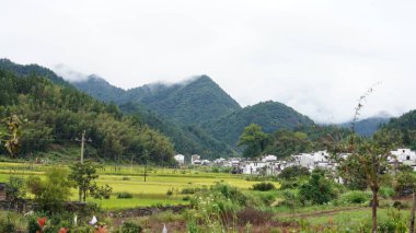 Yeşil ormanlı güzel dağlar ve yağmurlu günlerde arka planda kalan küçük köyler.