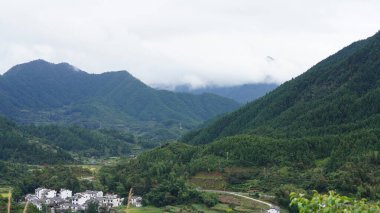 Yeşil ormanlı güzel dağlar ve yağmurlu günlerde arka planda kalan küçük köyler.
