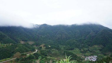 Yeşil ormanı olan güzel dağlar ve Çin kırsalının arka planında küçük bir köy.