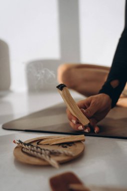 Yogini, Palo Santo 'yu elinde yoga minderiyle tutuyor.