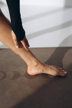 Yoga minderinin üzerinde ayak ve ayak parmaklarını geren bir kadının yakın plan fotoğrafı. Uzun kollu siyah bir bluz giyiyor ve esnemeye odaklanması esnekliğin önemini vurguluyor.