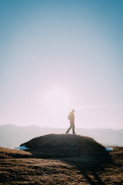 Güneşin doğuşunda tepede tek başına duran bir yürüyüşçünün çarpıcı görüntüsü. Sabahın erken saatlerinde ışık yumuşak, ruhani bir parıltı yaratır. Yürüyüşçünün siluetini engin gökyüzüne vurgular. Bu...