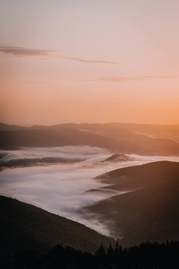 Yuvarlanan tepelerin üzerinde sisli bir güneşin doğuşunu yakalayan nefes kesici bir fotoğraf vadileri nazikçe kaplayan sis tabakalarıyla. Sabah gökyüzünün ılık renkleri kusursuz bir şekilde harmanlanır.