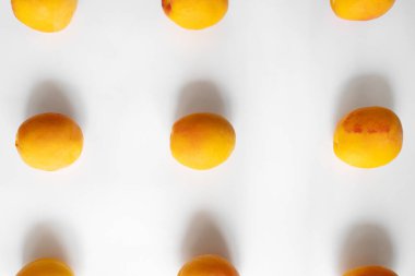 Bu dikey fotoğraf beyaz arka planda taze kayısıların temiz ve minimalist bir düzenini içerir. Kayısılar şebeke deseninde eşit aralıklarla aralıklarla, canlı turuncu renklerini gösteriyorlar.