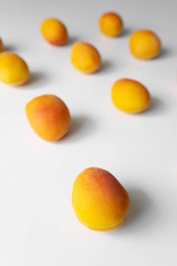 Bu dikey fotoğraf beyaz arka planda taze kayısıların temiz ve minimalist bir düzenini içerir. Kayısılar şebeke deseninde eşit aralıklarla aralıklarla, canlı turuncu renklerini gösteriyorlar.