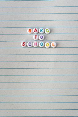 This image captures the phrase BACK TO SCHOOL creatively spelled out using colorful alphabet beads, placed neatly on a sheet of lined paper. The vibrant colors of the beads stand out against the clipart