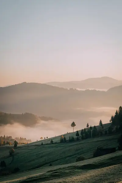 stock image A peaceful morning view of mist-covered valleys and rolling green hills under a soft sky, capturing the serene beauty of the countryside.