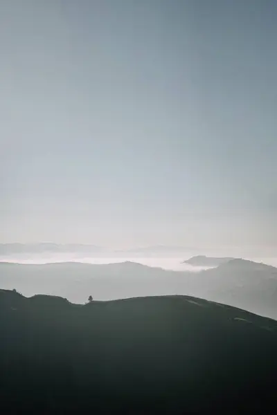 stock image A peaceful morning view of mist-covered valleys and rolling green hills under a soft sky, capturing the serene beauty of the countryside.