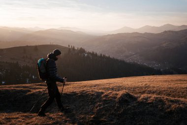 Gün batımında bir dağ sırtı boyunca tek başına yürüyen bir yürüyüşçü, geniş tepe ve vadilerden oluşan geniş bir manzaraya sahiptir. Sıcak, altın ışık sahnenin sükunetini arttırır..