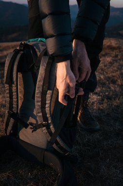 Altın saat boyunca otlak bir dağ sırtında yürüyüş malzemelerini büyük bir sırt çantasına koyan bir yürüyüşçünün yakın çekimi. Batan güneş sıcacık bir ışık saçıyor, açık hava macera takımlarını vurguluyor..