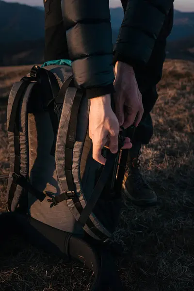 stock image Close-up of a hiker packing gear into a large backpack on a grassy mountain ridge during the golden hour. The setting sun casts warm light, highlighting the outdoor adventure gear.