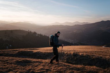 Gün batımında bir dağ sırtı boyunca tek başına yürüyen bir yürüyüşçü, geniş tepe ve vadilerden oluşan geniş bir manzaraya sahiptir. Sıcak, altın ışık sahnenin sükunetini arttırır..