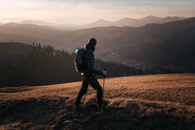 Gün batımında bir dağ sırtı boyunca tek başına yürüyen bir yürüyüşçü, geniş tepe ve vadilerden oluşan geniş bir manzaraya sahiptir. Sıcak, altın ışık sahnenin sükunetini arttırır..