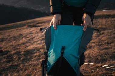 Altın saat boyunca otlak bir dağ sırtında yürüyüş malzemelerini büyük bir sırt çantasına koyan bir yürüyüşçünün yakın çekimi. Batan güneş sıcacık bir ışık saçıyor, açık hava macera takımlarını vurguluyor..