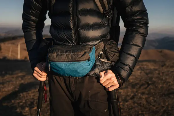 stock image A detailed close-up of a hikers gear, focusing on the waist pack and trekking poles, against the backdrop of a mountain landscape. The gear highlights the preparation and equipment needed for outdoor