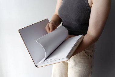 Bir kadın çizim defterinin boş sayfalarını karıştırır, yaratıcı fikirlere hazırdır. Temiz sayfalar, minimalist bir ortamda yaratıcılık, tasarım ve kişisel ifade potansiyelini ortaya koyuyor..