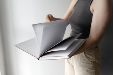 Bir kadın çizim defterinin boş sayfalarını karıştırır, yaratıcı fikirlere hazırdır. Temiz sayfalar, minimalist bir ortamda yaratıcılık, tasarım ve kişisel ifade potansiyelini ortaya koyuyor..