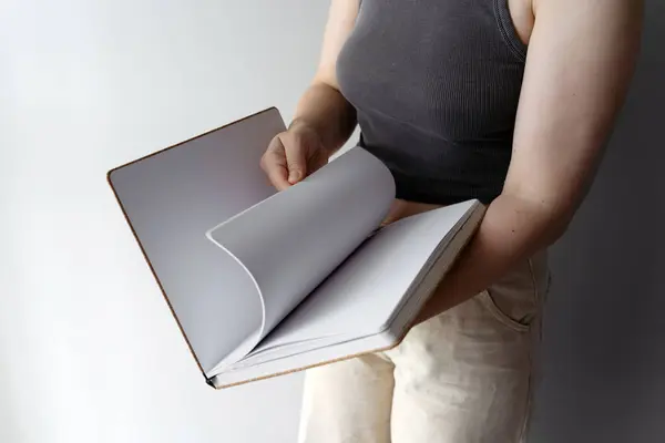 stock image A woman flips through the blank pages of a sketchbook, ready for creative ideas. The clean pages suggest potential for creativity, design, and personal expression in a minimalist setting.