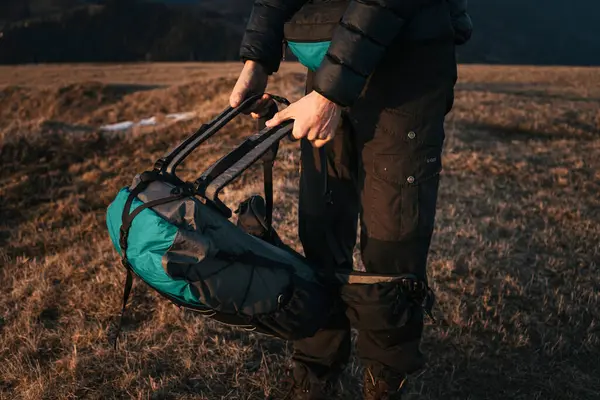 stock image Close-up of a hiker packing gear into a large backpack on a grassy mountain ridge during the golden hour. The setting sun casts warm light, highlighting the outdoor adventure gear.