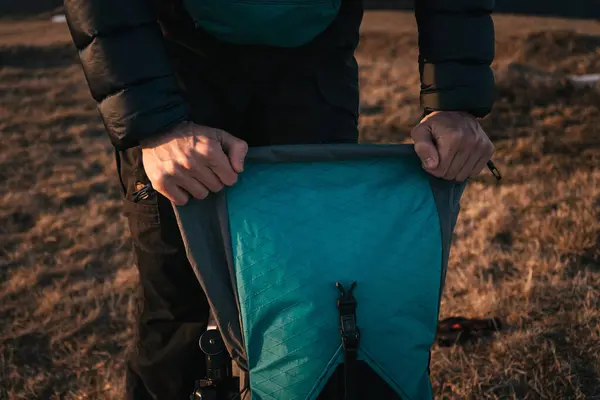 stock image Close-up of a hiker packing gear into a large backpack on a grassy mountain ridge during the golden hour. The setting sun casts warm light, highlighting the outdoor adventure gear.