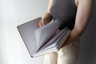Bir kadın çizim defterinin boş sayfalarını karıştırır, yaratıcı fikirlere hazırdır. Temiz sayfalar, minimalist bir ortamda yaratıcılık, tasarım ve kişisel ifade potansiyelini ortaya koyuyor..