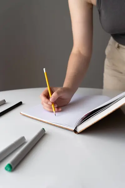 stock image A close-up of a womans hand holding a yellow pencil while writing in a blank notebook. The scene symbolizes creativity, fresh ideas, and the concept of a new beginning or project.