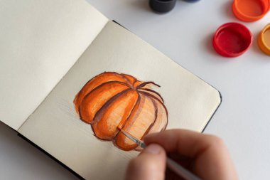Sanatçı balkabağı resimlerine son rötuşlarını dikkatlice gouache boyaları kullanarak uygular. Canlı renklerin olduğu kavanozlar masanın üzerine yayılıyor ve yaratıcı süreci gösteriyor..