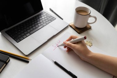 Bir dizüstü bilgisayar, kahve fincanı, defter, kalem ve kalemle beyaz bir masanın üzerine kurulmuş temiz ve minimalist bir ofis. Üretkenlik, uzak çalışma ve yaratıcı planlama için mükemmel..