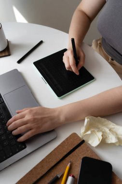 Dizüstü bilgisayar, defter, çizim tableti ve kahvenin yer aldığı yaratıcı bir çalışma alanı. Buruşmuş kağıt, yaratıcı süreç boyunca beyin fırtınası ve başarısız fikirleri sembolize eder..