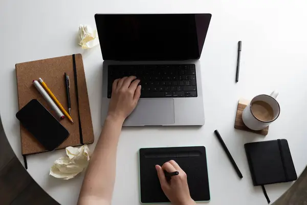 stock image A top view of a creative workspace featuring a laptop, notebook, drawing tablet, and coffee. Crumpled paper symbolizes brainstorming and unsuccessful ideas during the creative process.