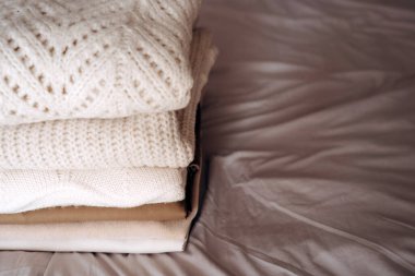 Yumuşak, nötr tonlarda düzgün örülü kazaklar bir yatakta oturur. Süveter dokuları ve desenleri sıcaklığı ve konforu iletir. Sürdürülebilir moda ve ikinci el kıyafetleri desteklemek için mükemmeldir.