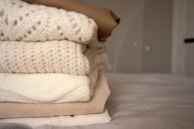 Yumuşak, nötr tonlarda düzgün örülü kazaklar bir yatakta oturur. Süveter dokuları ve desenleri sıcaklığı ve konforu iletir. Sürdürülebilir moda ve ikinci el kıyafetleri desteklemek için mükemmeldir.