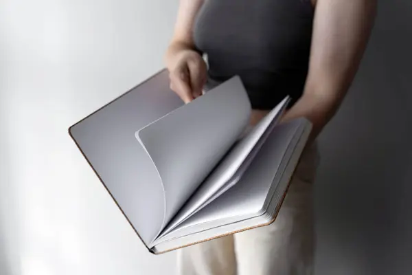 stock image A woman holding a pencil over a blank notebook while sitting at a table near a window. The scene symbolizes creativity, new beginnings, and inspiration in a calm and peaceful environment.