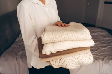 Tarafsız tonlarda katlanmış örgü süveter tutan bir kadın. Sürdürülebilir moda, ikinci el giysi ve minimalist yaşam tarzı kavramları için mükemmel bir imaj..