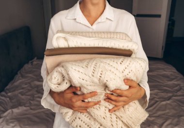 Tarafsız tonlarda katlanmış örgü süveter tutan bir kadın. Sürdürülebilir moda, ikinci el giysi ve minimalist yaşam tarzı kavramları için mükemmel bir imaj..