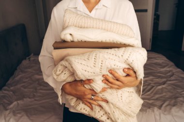 Tarafsız tonlarda katlanmış örgü süveter tutan bir kadın. Sürdürülebilir moda, ikinci el giysi ve minimalist yaşam tarzı kavramları için mükemmel bir imaj..