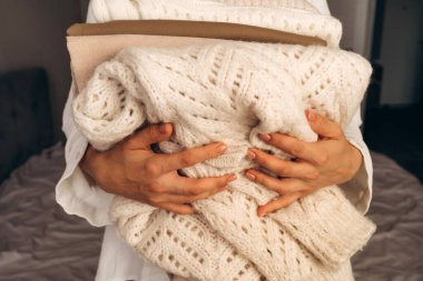 Tarafsız tonlarda katlanmış örgü süveter tutan bir kadın. Sürdürülebilir moda, ikinci el giysi ve minimalist yaşam tarzı kavramları için mükemmel bir imaj..