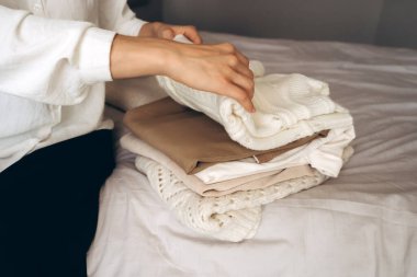 Sade örgü ve nötr renkli giysileri yatağa katlayan, minimalist ve sürdürülebilir bir moda yaklaşımı sergileyen biri. Ev organizasyonu, konfor ve çevre dostu yaşam tarzı temaları için ideal.