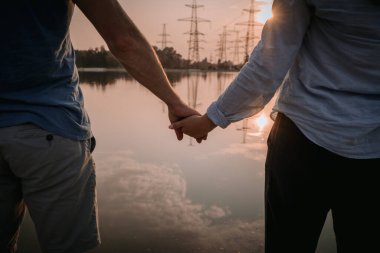  Gün batımında gölün sakin sularında el ele tutuşan bir çift olarak huzurlu bir an. Uzaktan yansıyan elektrik hatlarıyla. Altın ışık romantik ve sakin bir atmosfer yaratır..