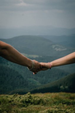 A close-up of two hands with an engagement ring, set against a stunning backdrop of lush green mountains. The serene landscape symbolizes love, connection, and the promise of a future together. clipart