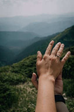 A close-up of two hands with an engagement ring, set against a stunning backdrop of lush green mountains. The serene landscape symbolizes love, connection, and the promise of a future together. clipart