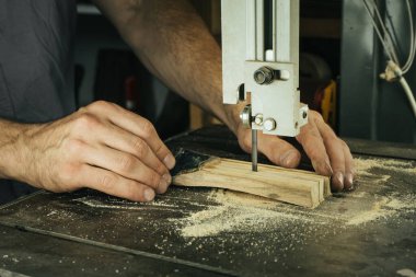 Tahta bir parça yapmak için testere kullanan yetenekli bir marangozun yakın çekimi. Sanatçının elleri ahşabı bıçağın içinden geçirir, atölyedeki talaşlarla çevrili..