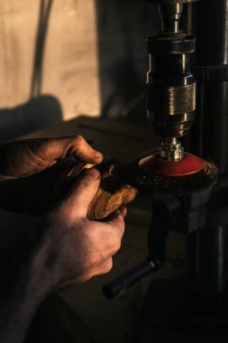 Elektrikli bir aletle cilalanan ahşap bir nesneyi tutan ellerin yakın çekimi. Ilık ışıklandırma, işçilik, hassasiyet ve ayrıntılı ahşap işçiliği sürecine odaklanmamızı sağlıyor..